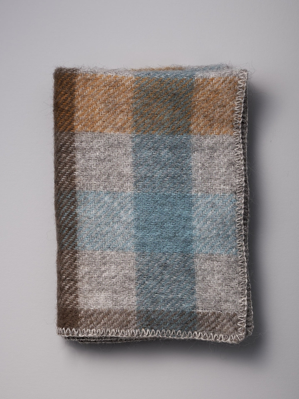 A Klippan Gotland Wool Baby Throw - Multi Turquoise blanket on a white surface.