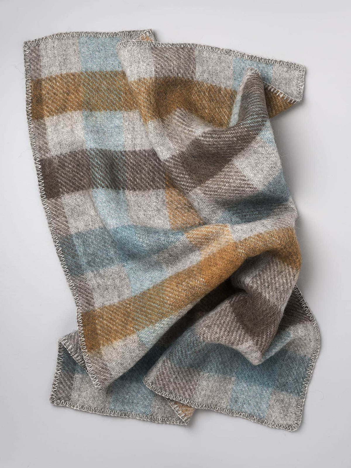 A Klippan Gotland Wool Baby Throw – Multi Turquoise blanket on a white surface.