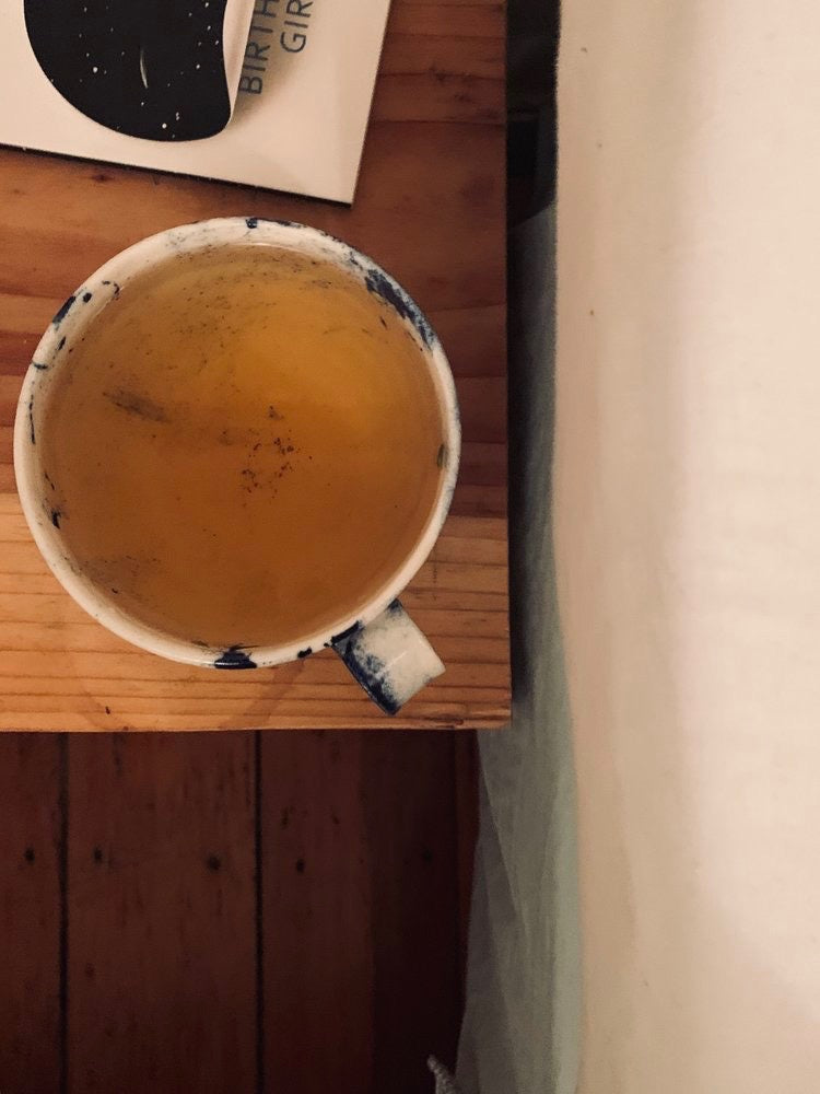 A cup of Kawakawa Vitality tea sits on a bed next to a book, brand name: Kaputi Studio.