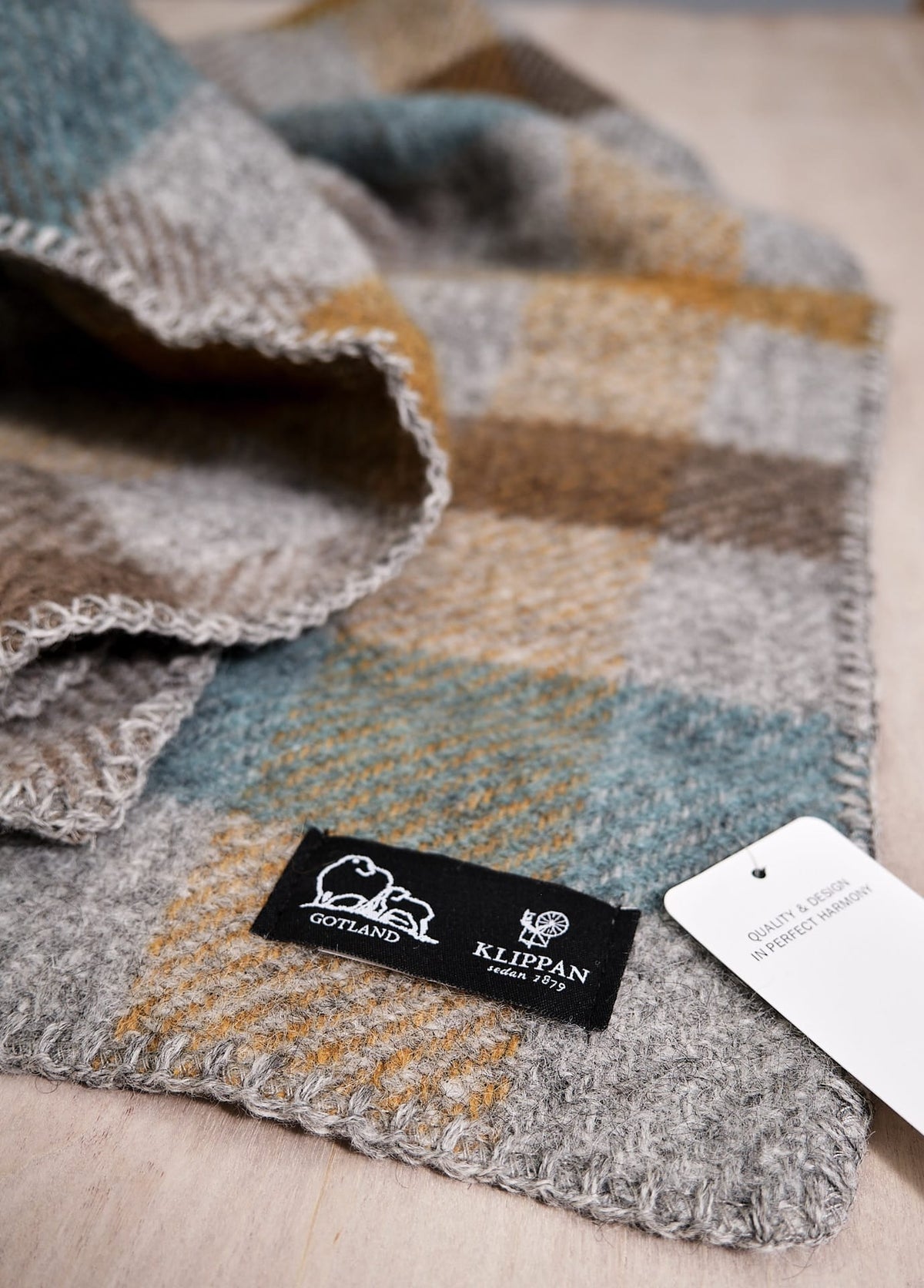 A Klippan Gotland Wool Baby Throw – Multi Turquoise with a tag on it is sitting on a table.