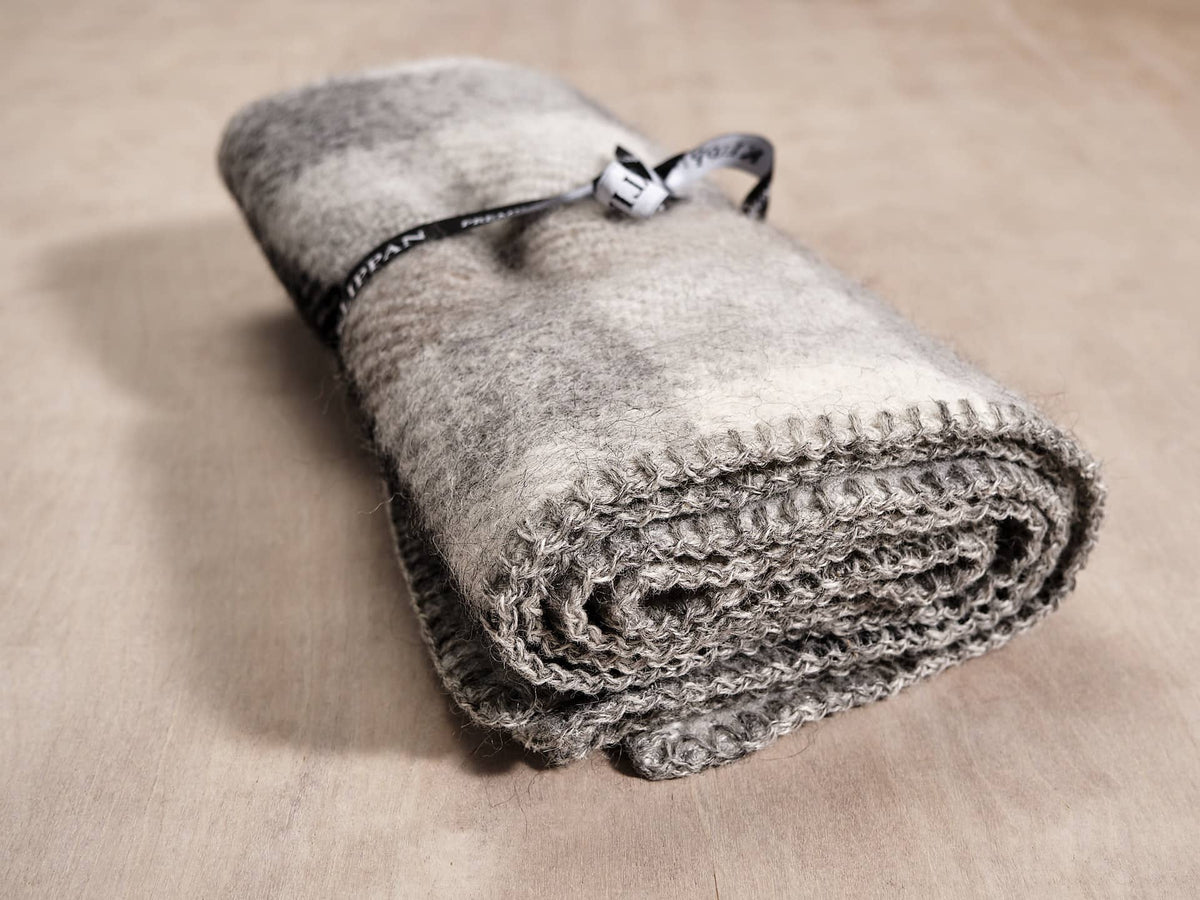 A Gotland Wool Baby Throw – Multi Grey blanket by Klippan on top of a wooden table.