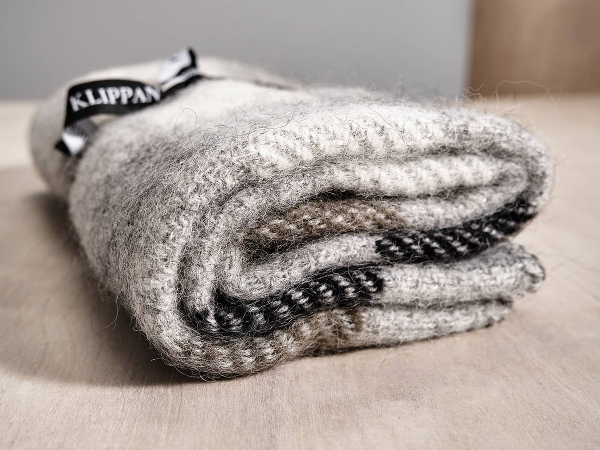 A Klippan Gotland Wool Baby Throw – Multi Grey blanket on top of a wooden table.