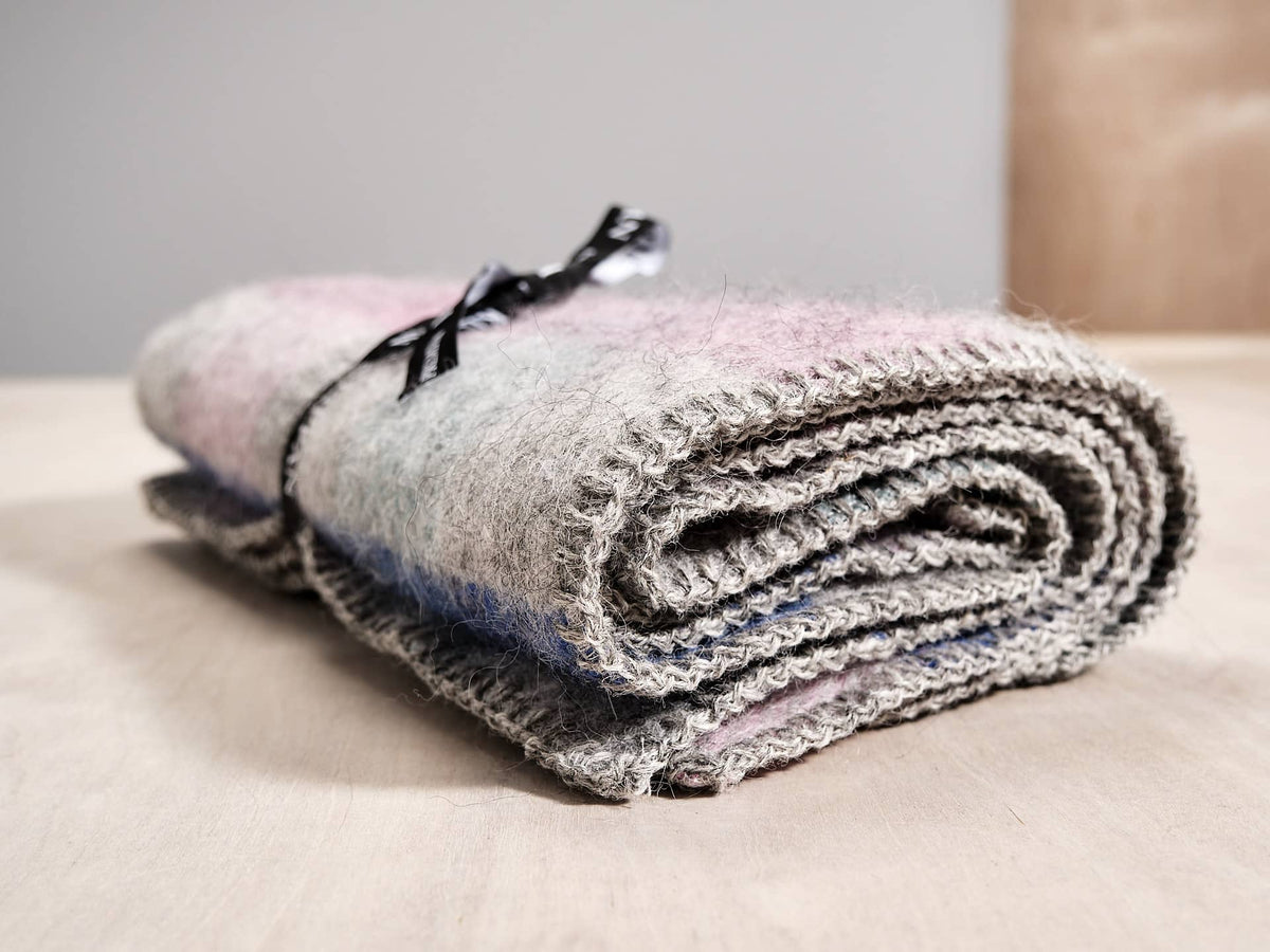 A Gotland Wool Baby Throw – Multi Pastel by Klippan on top of a wooden table.