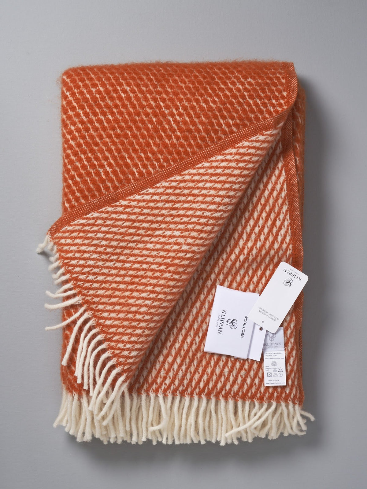 A Honeycomb ECO* Lambswool Throw – Rust by Klippan on a grey background.