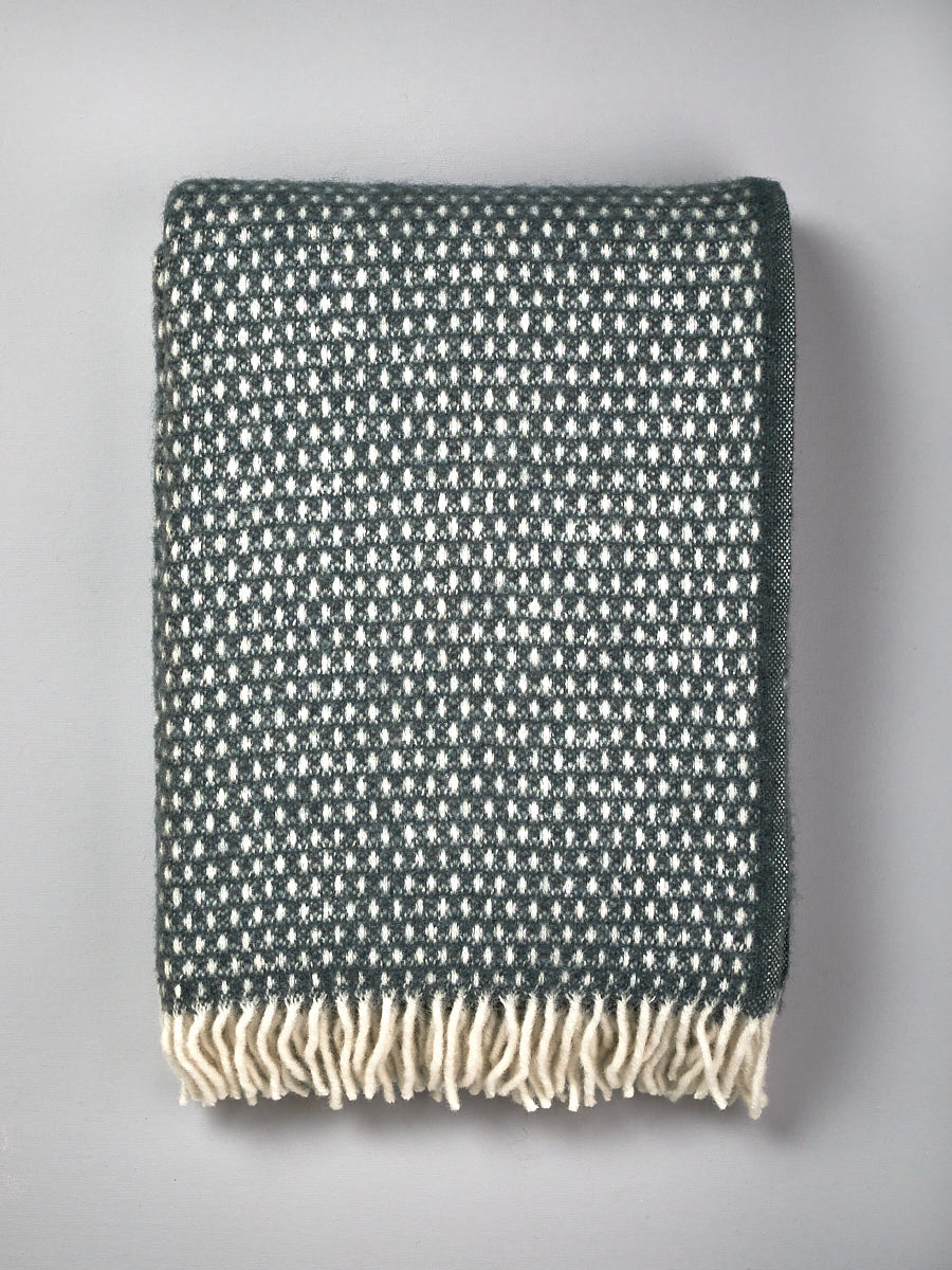 A Klippan Knut Woven Wool Throw - Balsam Green on a grey background.