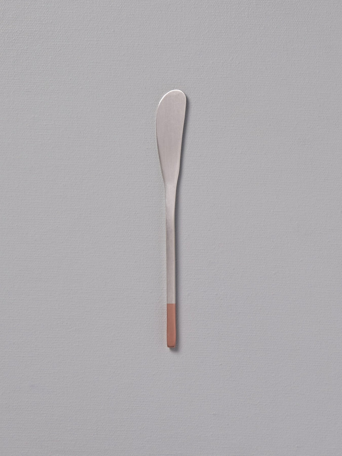 A Copper &amp; Stainless Steel Butter Knife by Kobo Aizawa sitting on a gray surface.