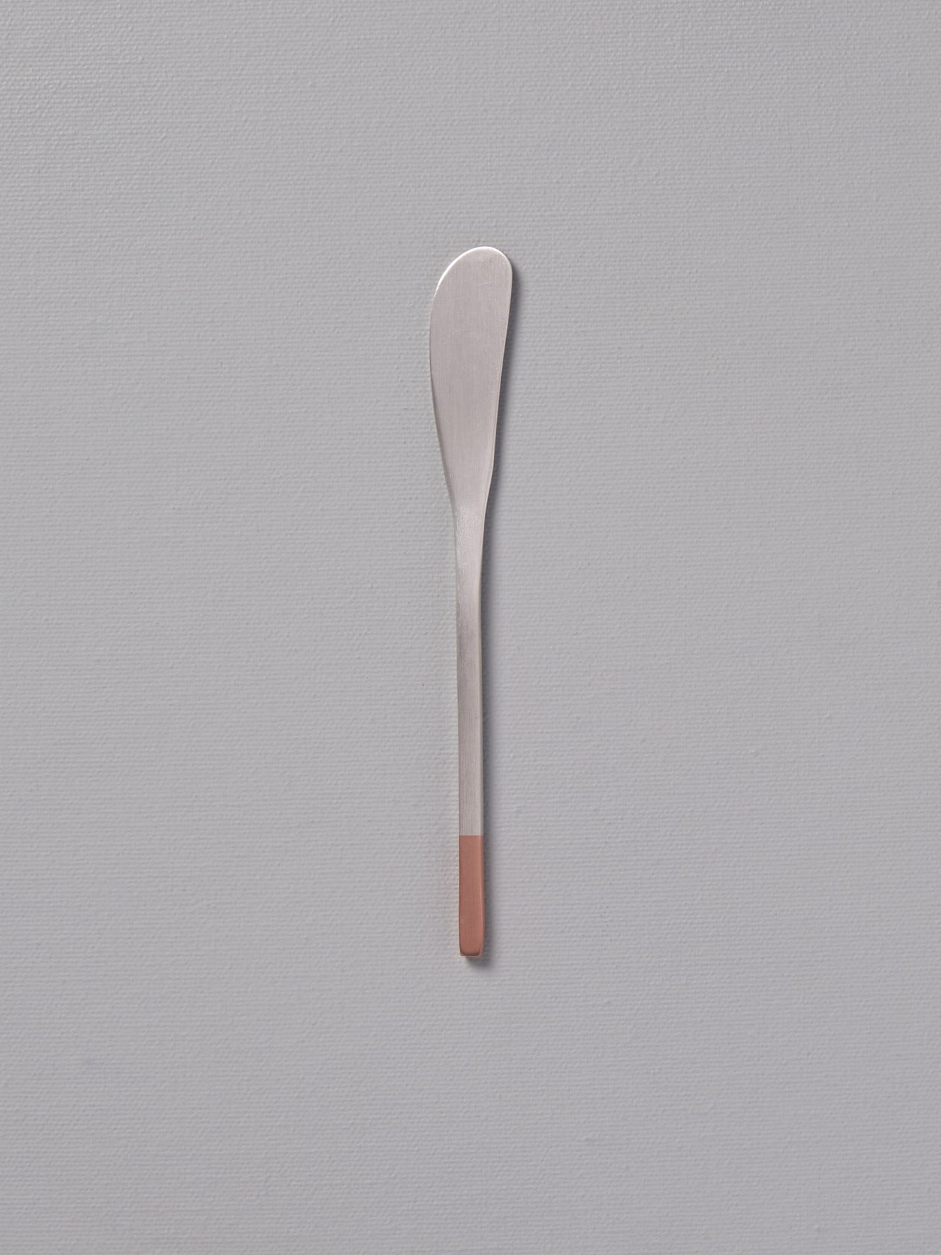 A Copper & Stainless Steel Butter Knife by Kobo Aizawa sitting on a gray surface.