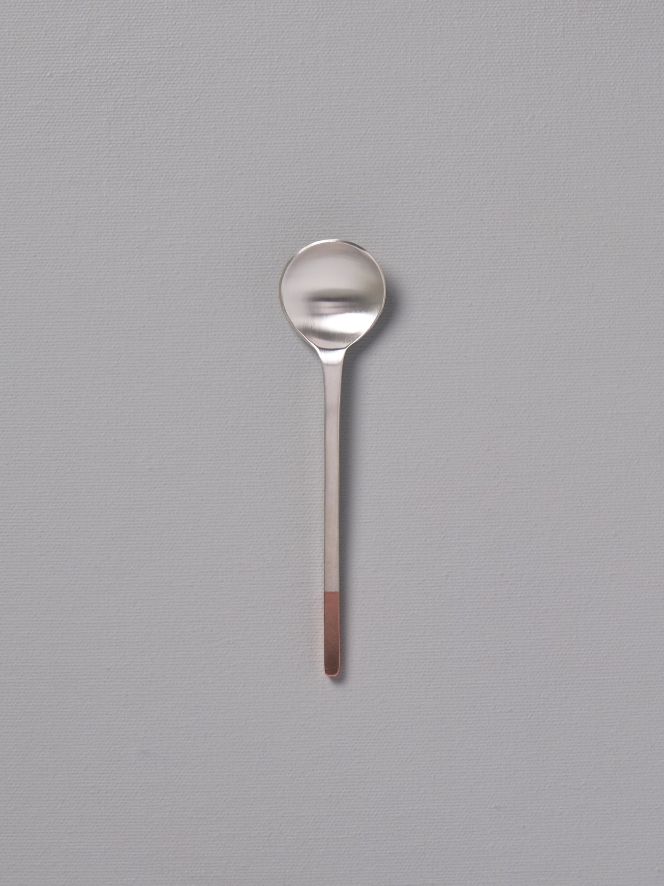 A small Copper and Stainless Steel Teaspoon by Kobo Aizawa on a grey background.