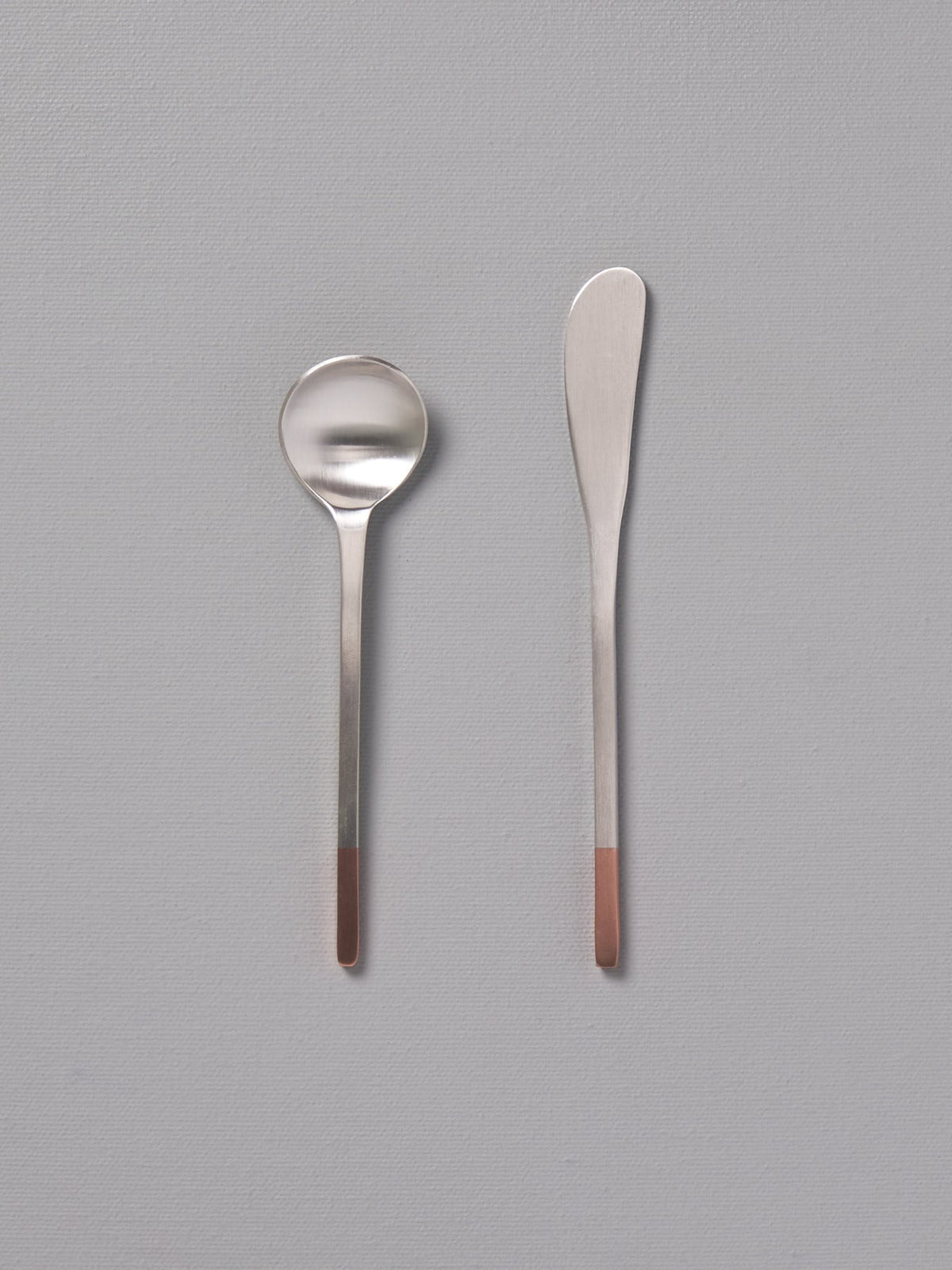 Two Copper and Stainless Steel Teaspoons by Kobo Aizawa on a grey surface.