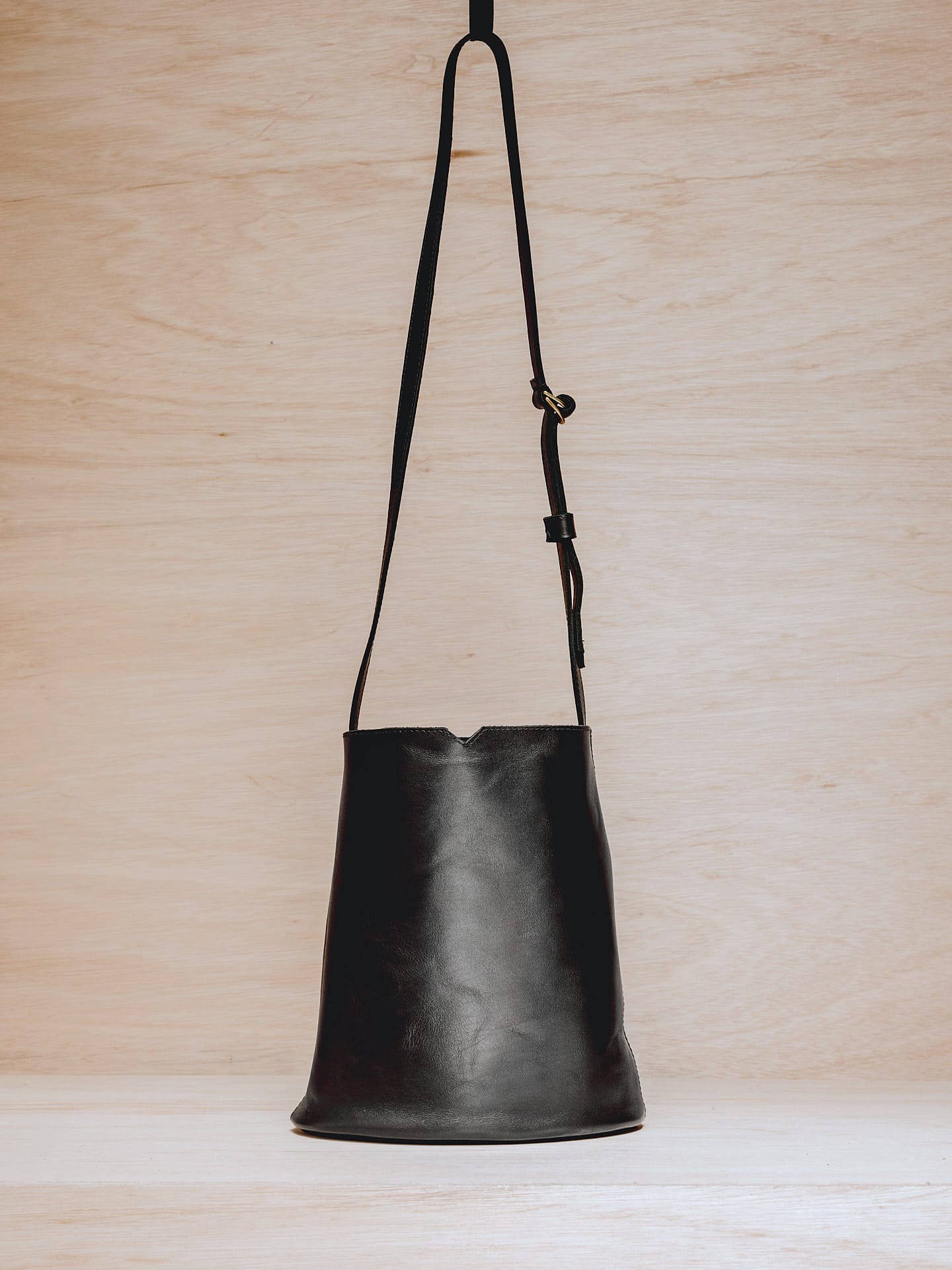 A Lets Dance black leather bucket bag hanging on a wooden wall.
