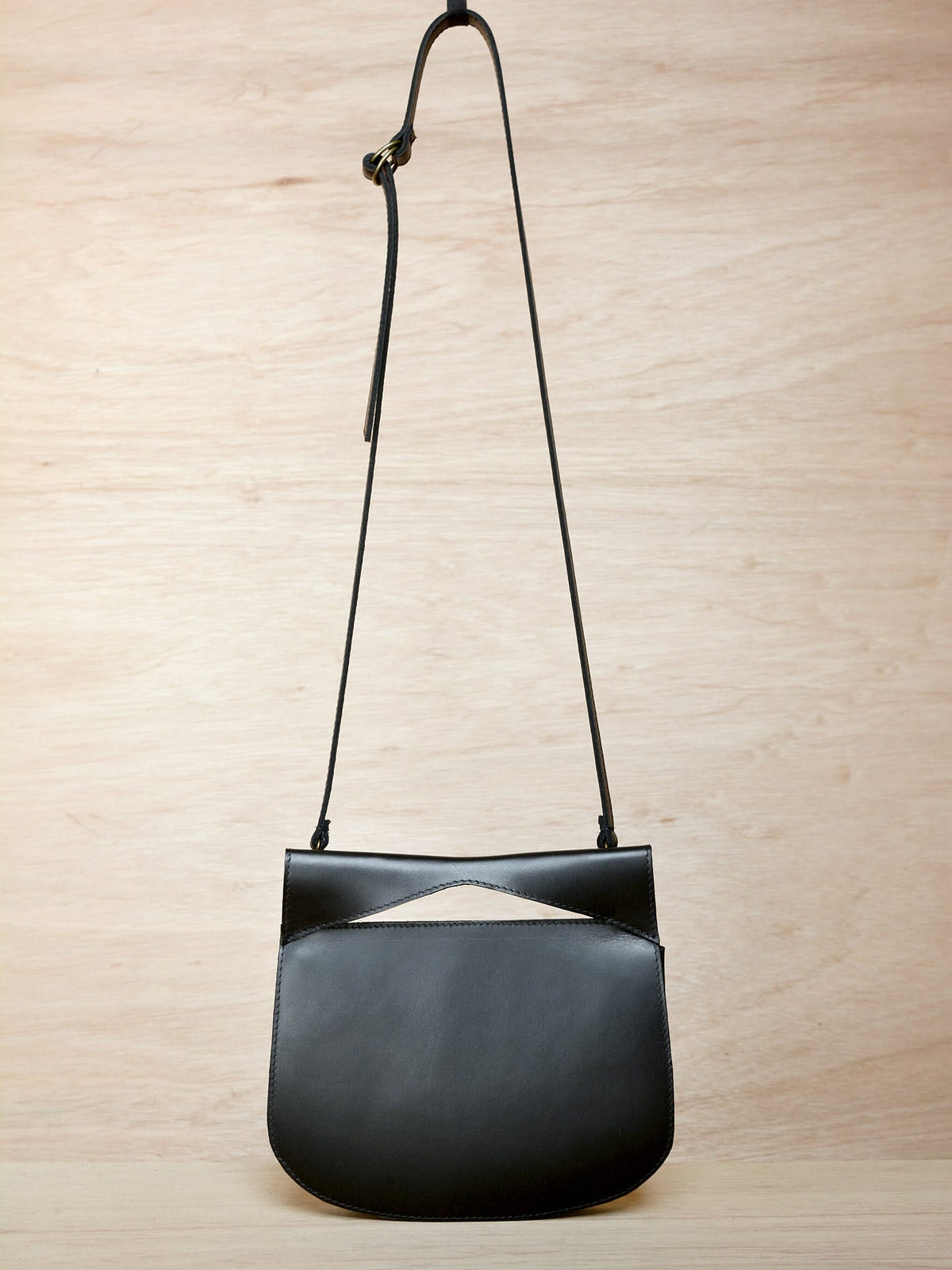 A black leather Cat bag hanging on a wooden wall. (Brand: Kohl &amp; Co)