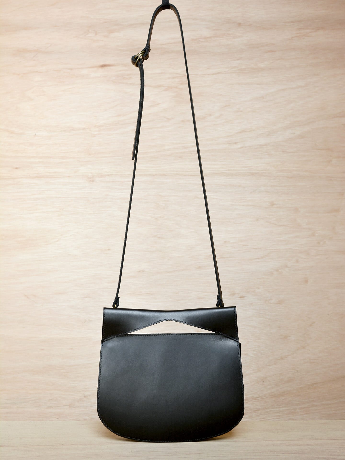 A black leather Cat bag hanging on a wooden wall. (Brand: Kohl & Co)