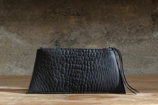 A Maya Carry - Black clutch bag by Kohl &amp; Co on a wooden table.