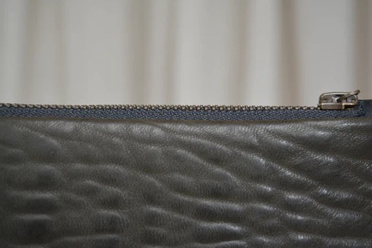 A close up of a Maya Clutch – Moss by Kohl &amp; Co grey leather zippered pouch.