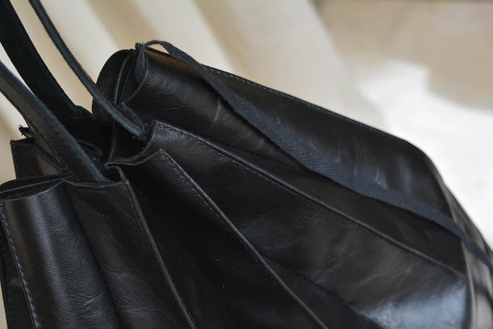 A black leather Pleats bag hanging on a curtain. (Brand Name: Kohl &amp; Co)