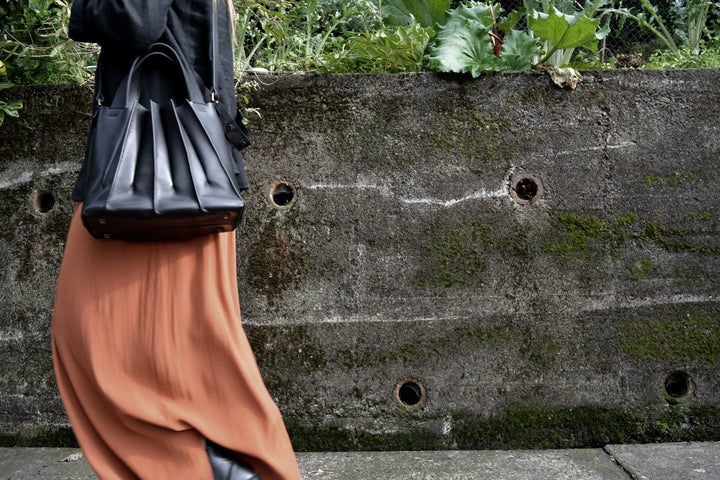 A woman wearing an orange Pleats Petite skirt and black Kohl &amp; Co bag.