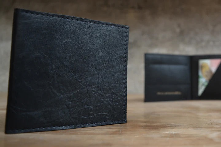 A black leather Kohl &amp; Co Skinny Wallet sitting on a wooden table.