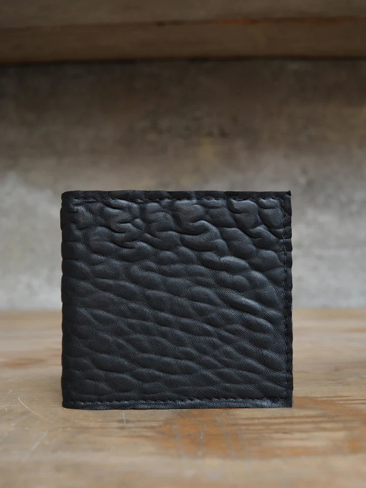 A black leather Kohl & Co Skinny Wallet sitting on top of a wooden table.