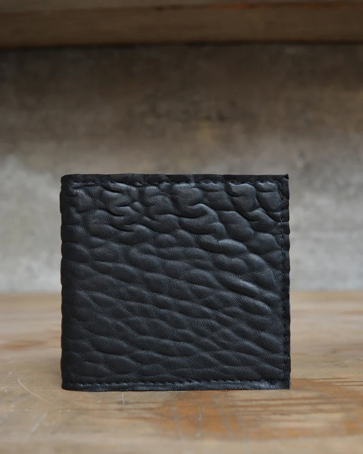 A black leather Kohl & Co Skinny Wallet sitting on top of a wooden table.