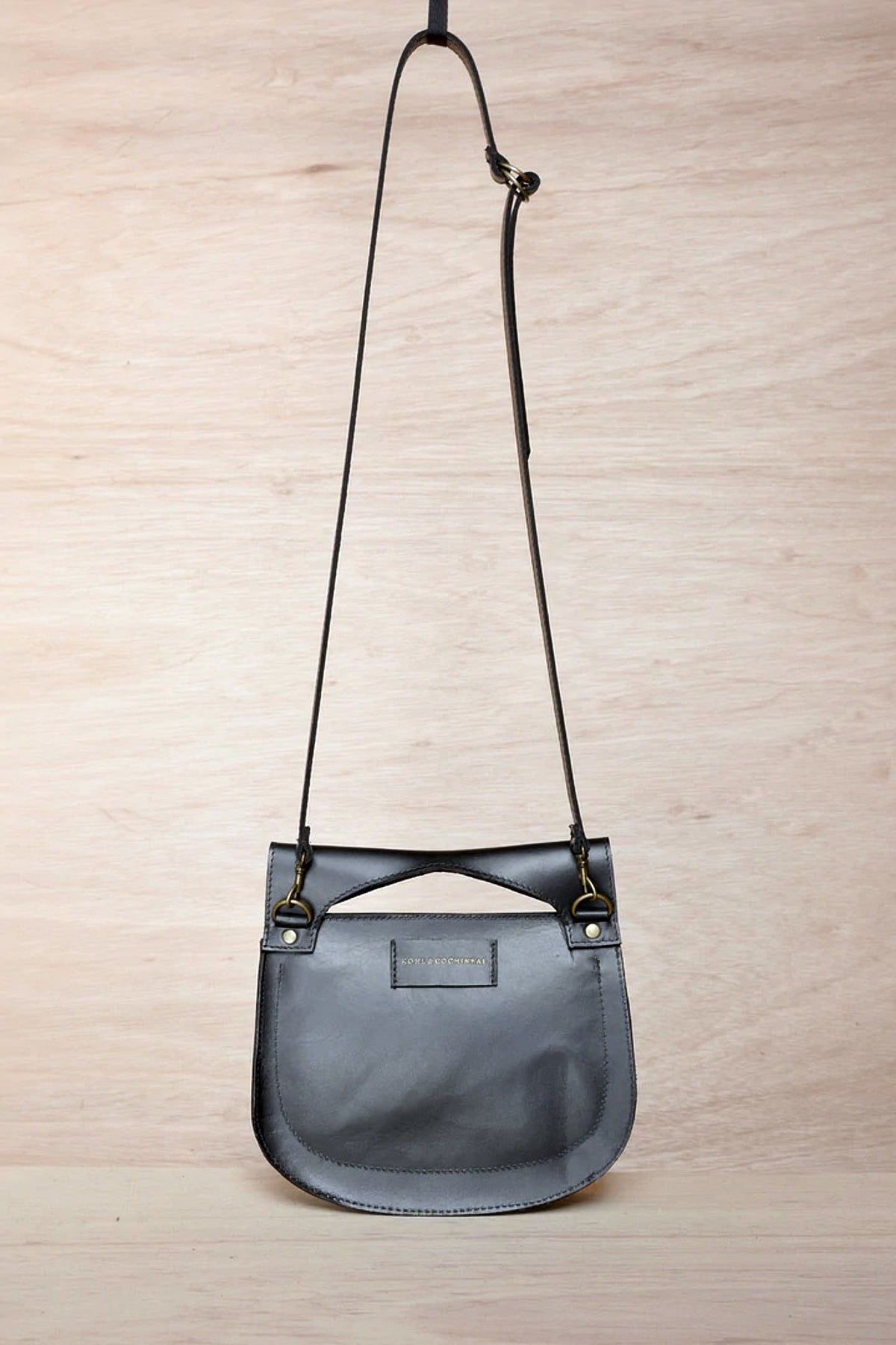 A small grey leather Cat bag hanging on a wooden wall.