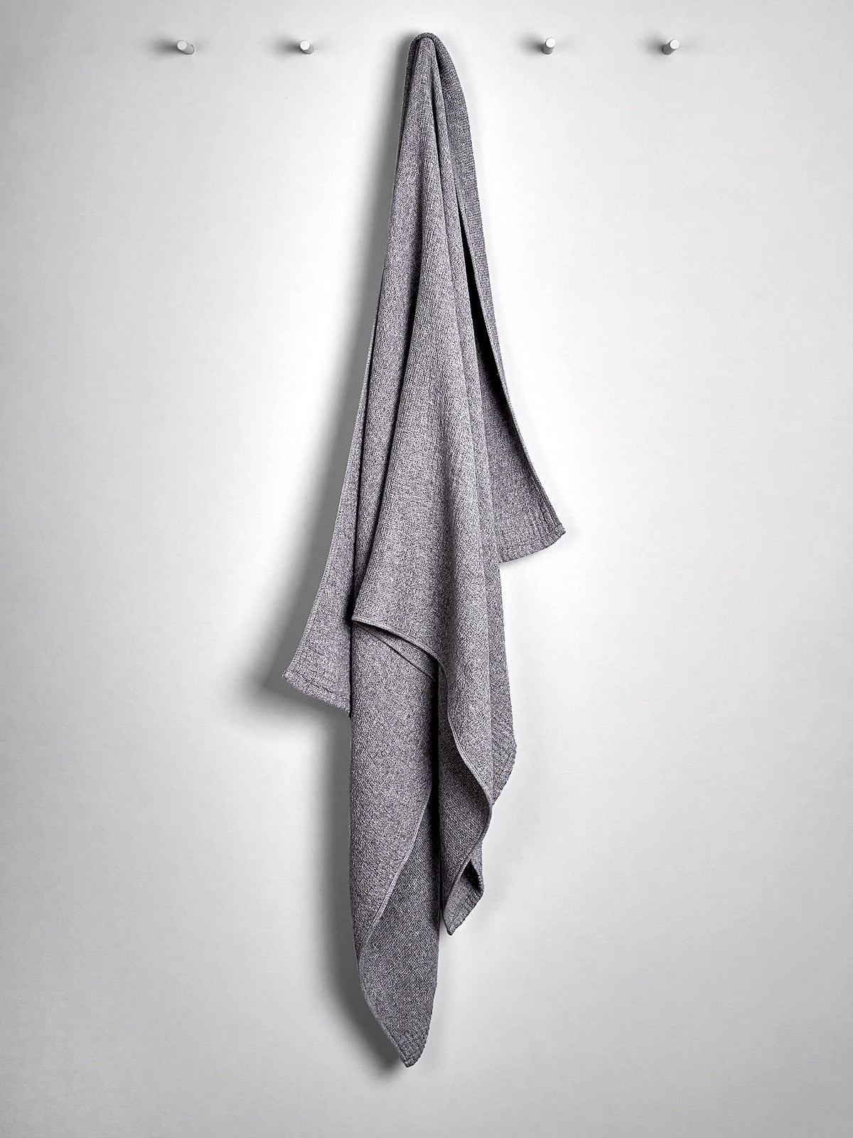 A gray Lana hand towel hanging on a hook against a light-colored wall. (Brand name: Kontex)