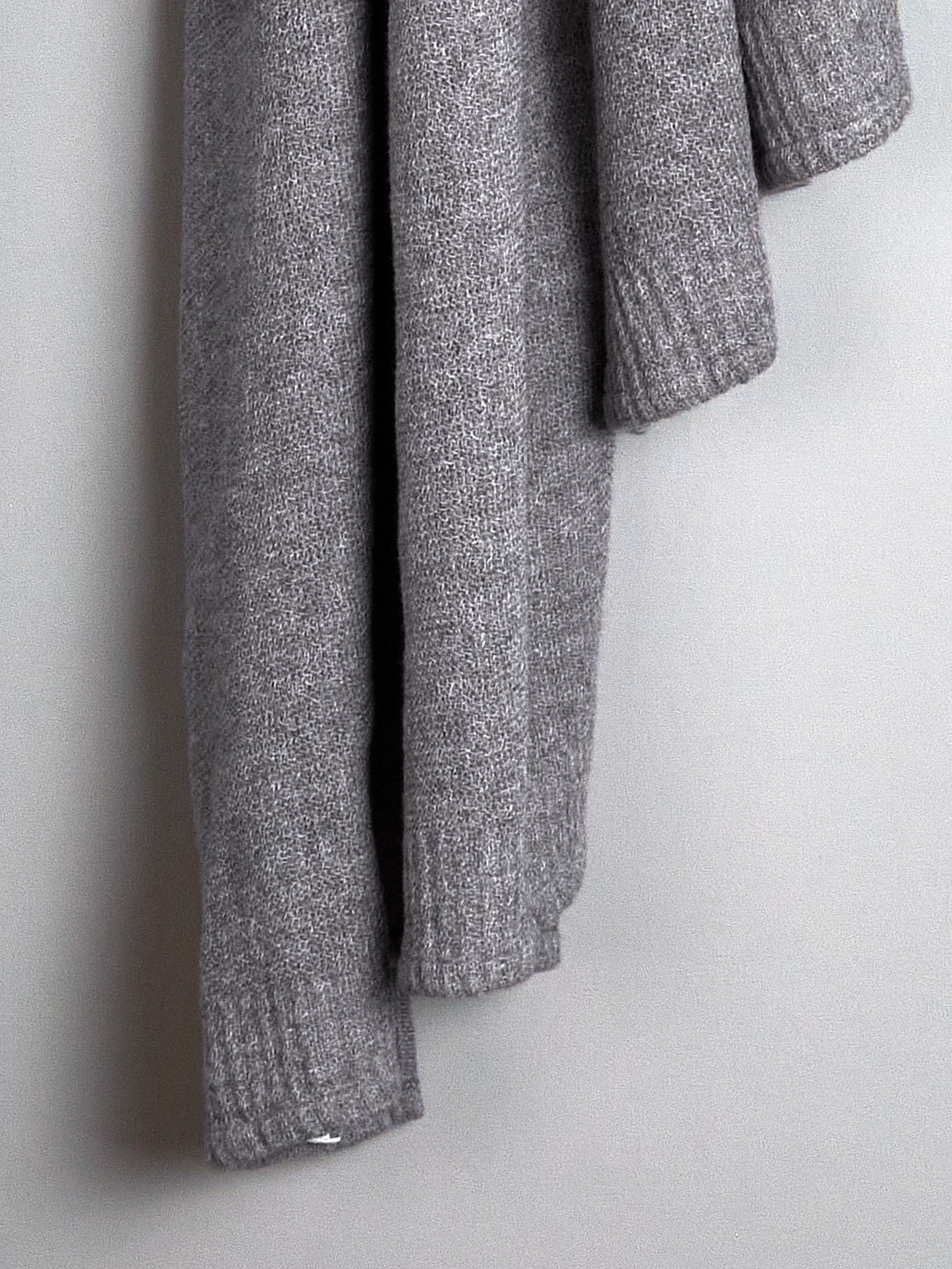 A grey knitted sweater hanging on a Kontex hand wall hook.