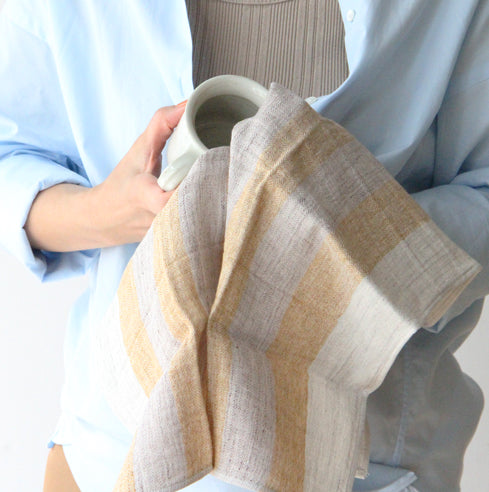 A woman is holding a Kontex Linen Tea Towel – Yellow or Navy with a striped pattern.