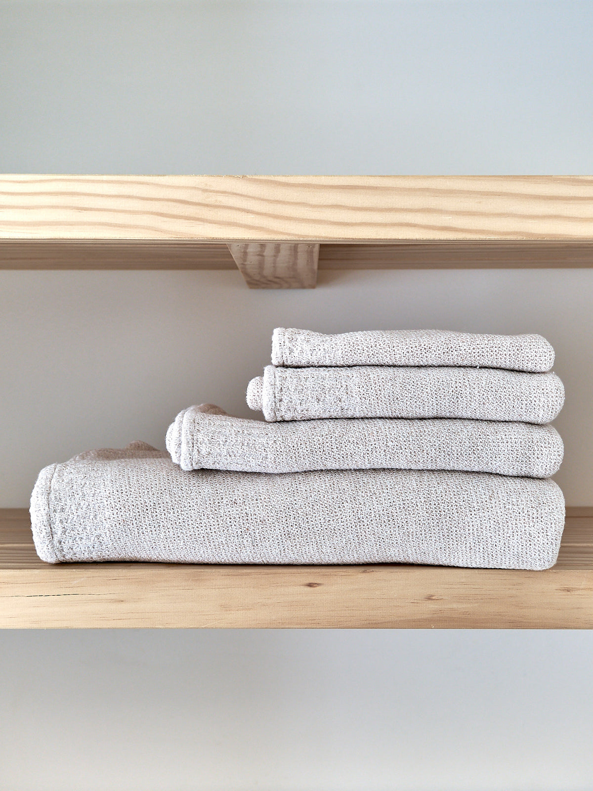 Neatly folded grey towels from the Kontex Re.Lana towel collection on a wooden shelf.