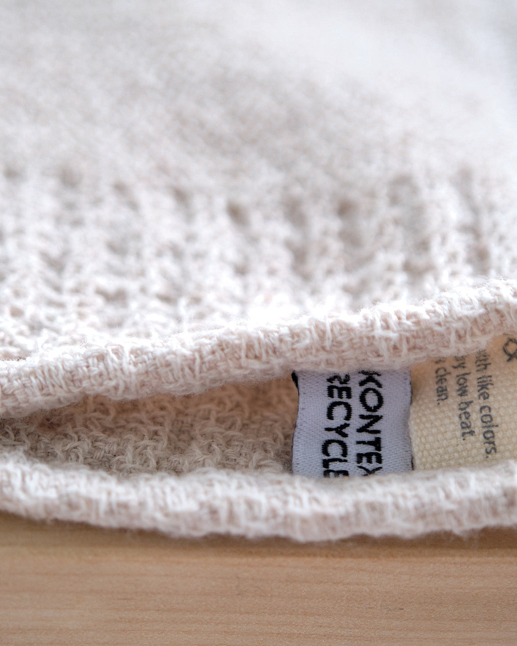 A neatly stacked set of three Kontex Re.Lana Towels from their Bath ⋄ Hair ⋄ Hand ⋄ Face collection, crafted from recycled cotton in beige hues, rests on a gray surface.