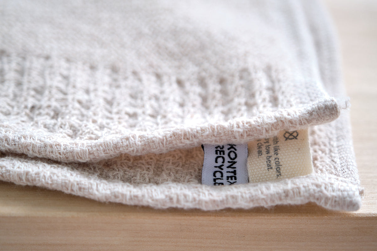 Close-up of a fabric label on a Re.Lana towel from the Kontex towel collection indicating the material, which upcycles discarded cotton using slow Japanese looms, is recyclable.