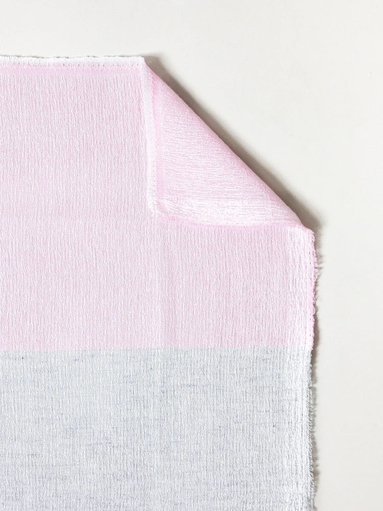 A folded piece of pink and white fabric, made in Imabari with a textured surface, is a highly absorbent Kontex Shukin Towel – Two Tone Grey ⋄ Pink.