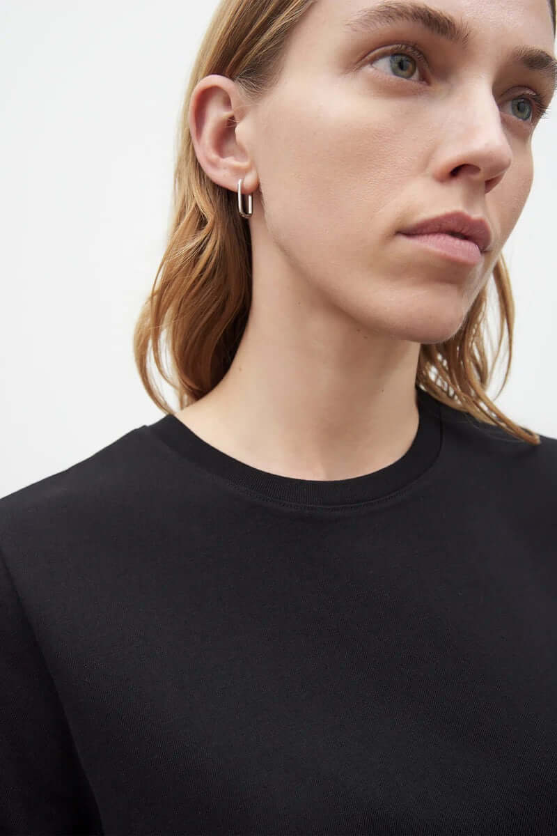 A model wearing a Kowtow A-Line Tee – Black and earrings.