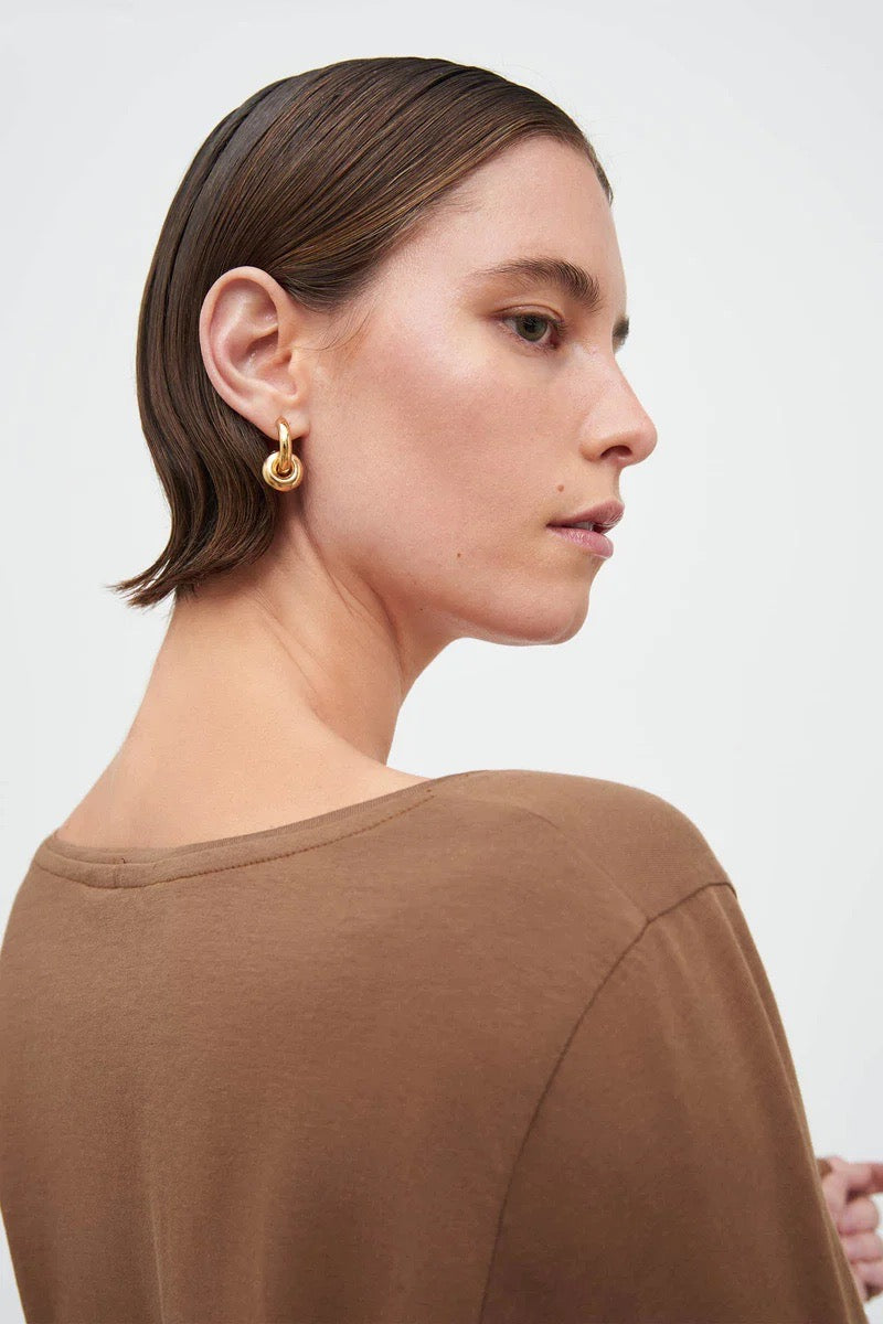 The back view of a woman wearing a Ballet Top - Earth by Kowtow and earrings.