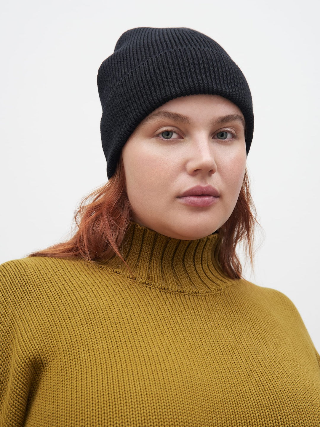 A woman wearing a yellow turtleneck and Kowtow black beanie.