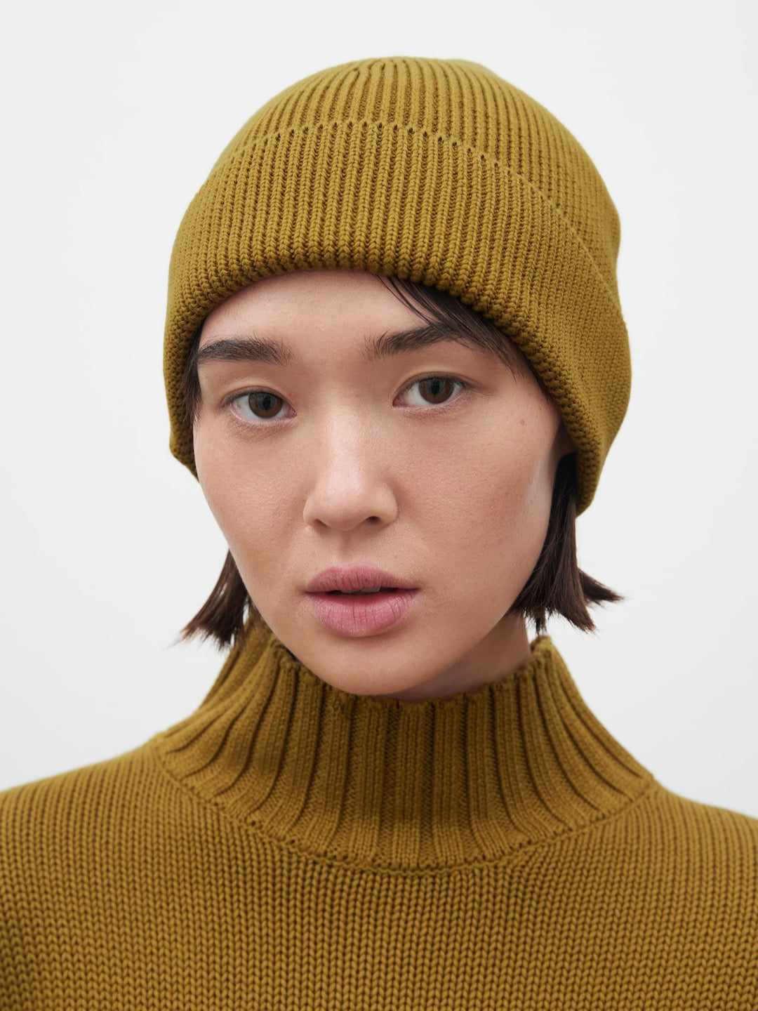 A woman wearing a mustard turtleneck sweater and Kowtow Chartreuse beanie.