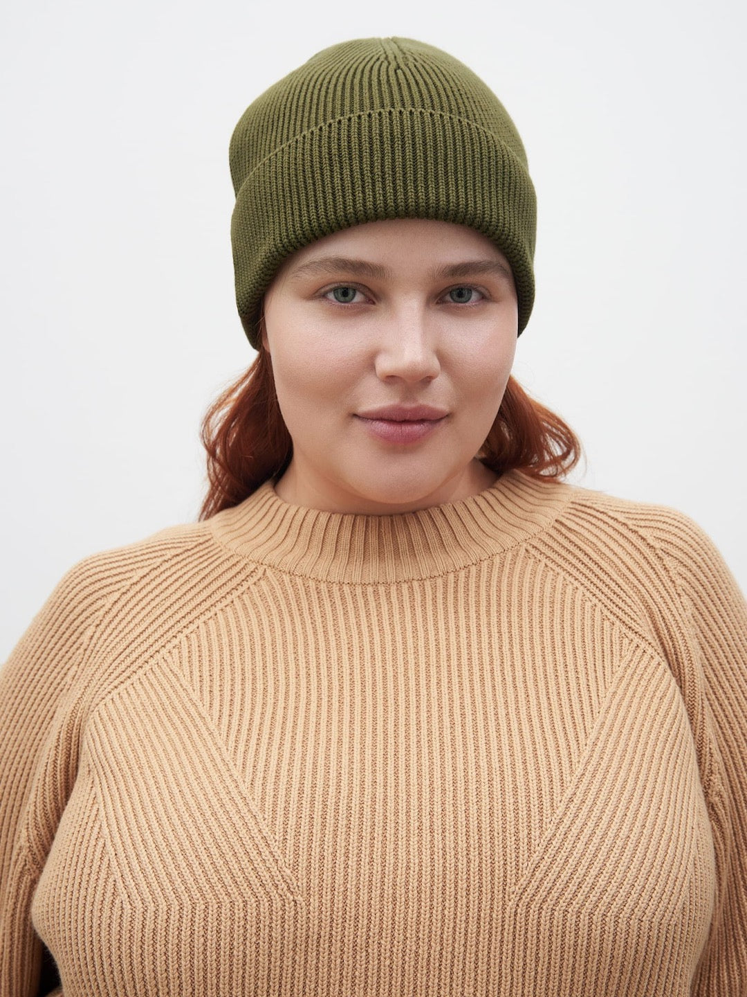 A woman wearing a tan sweater and Kowtow Moss beanie.