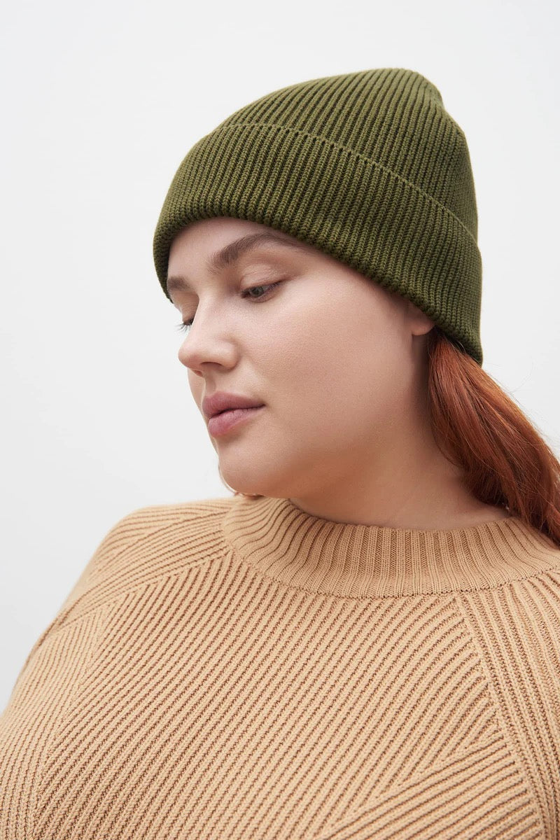 A woman wearing a green ribbed Kowtow beanie – Moss.