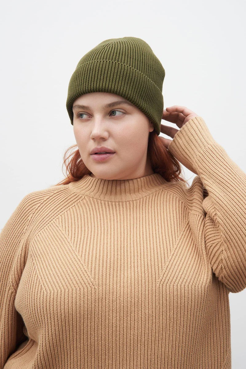 A model wearing a tan sweater and Moss beanie by Kowtow.