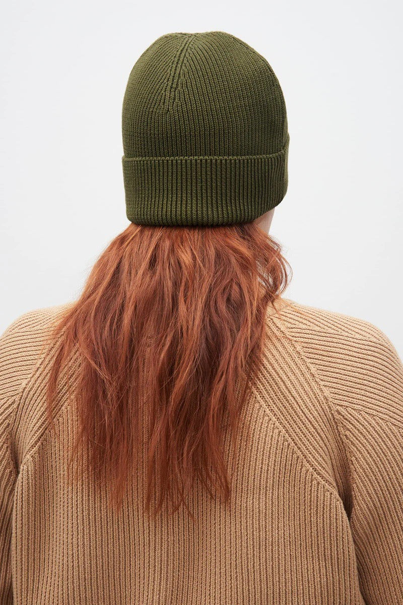 The back view of a woman wearing a green knit Kowtow beanie – Moss.