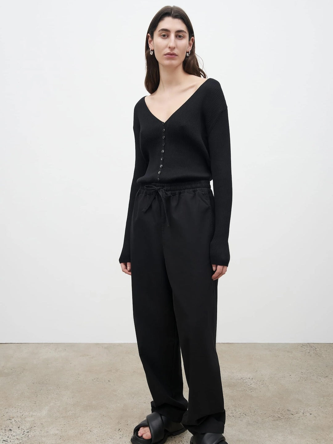 The model is wearing a black v - neck sweater and Kowtow's Blake Pants – Black.
