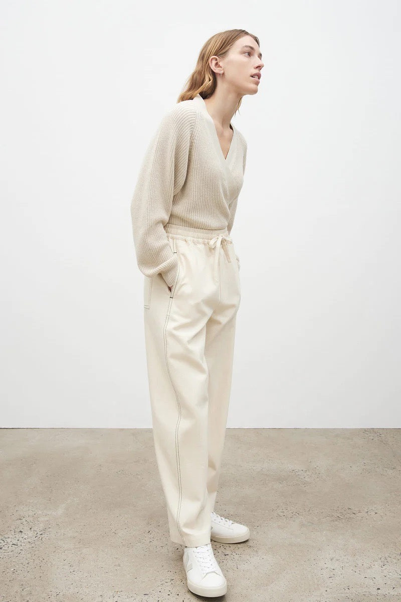 The model is wearing a white sweater and Kowtow Blake Pants – Greige.