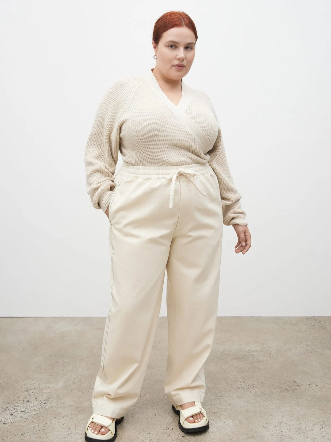 The model is wearing a cream sweater and Kowtow Blake Pants – Greige.
