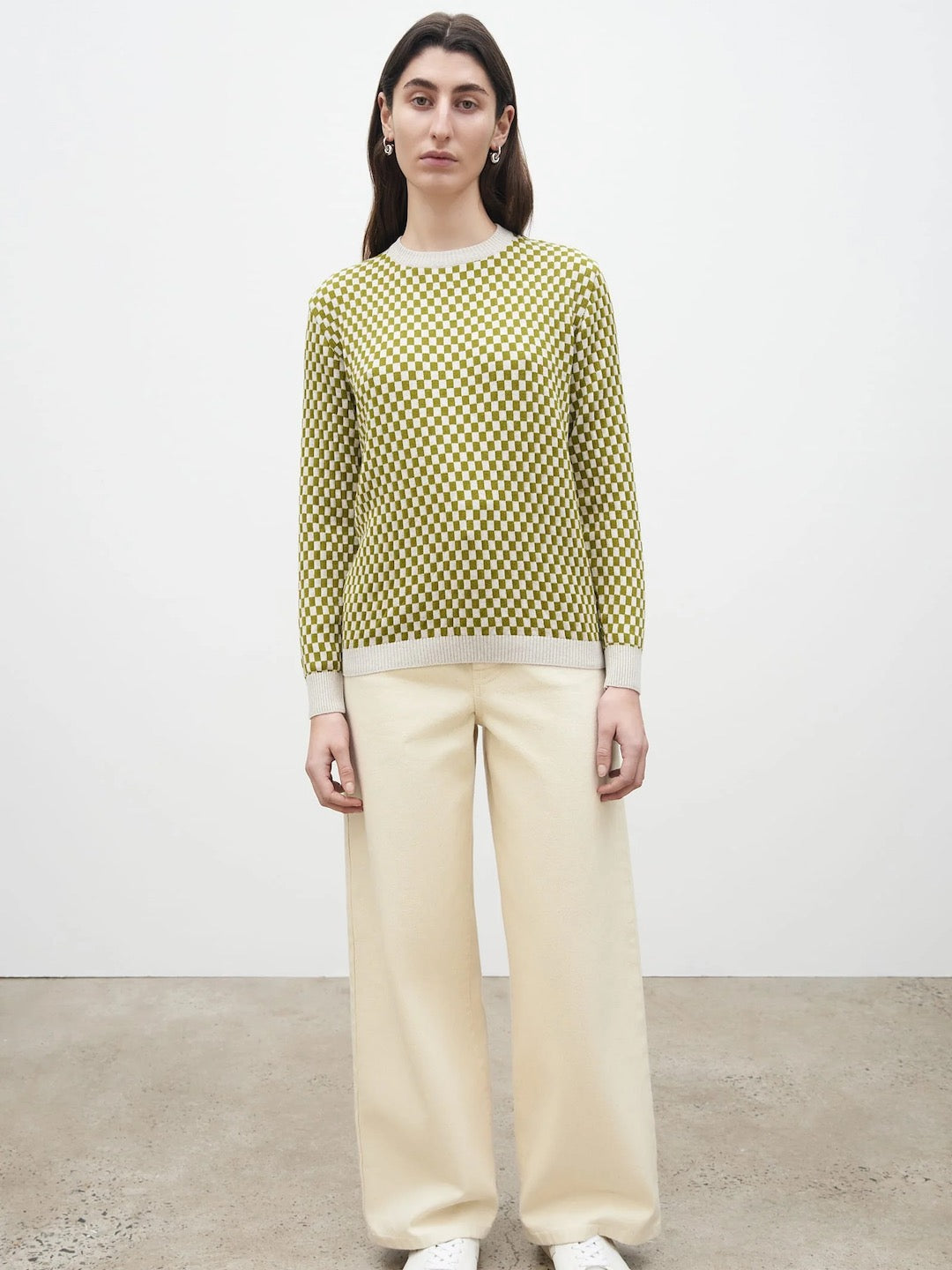 The model is wearing a Kowtow Checkerboard Knit Crew – Lawn Check sweater and cream wide leg pants.