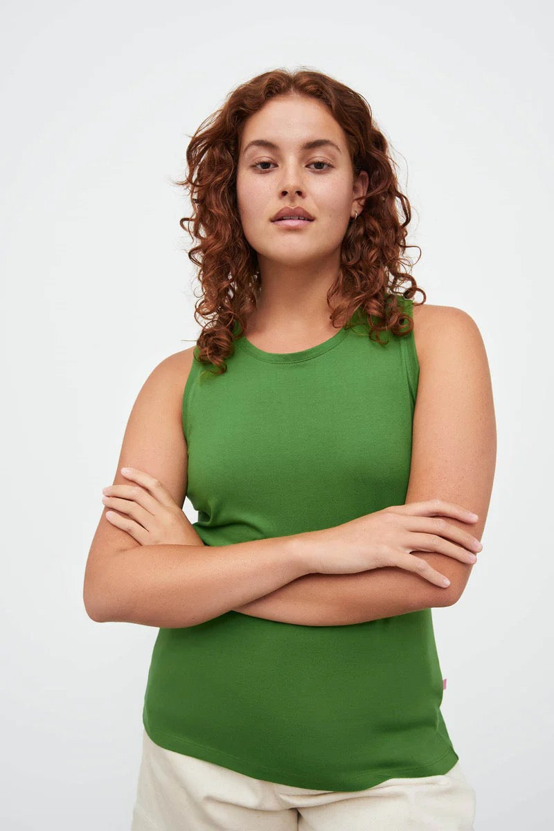 A woman wearing a Cross Back Singlet - Bright Green by Kowtow and white pants.