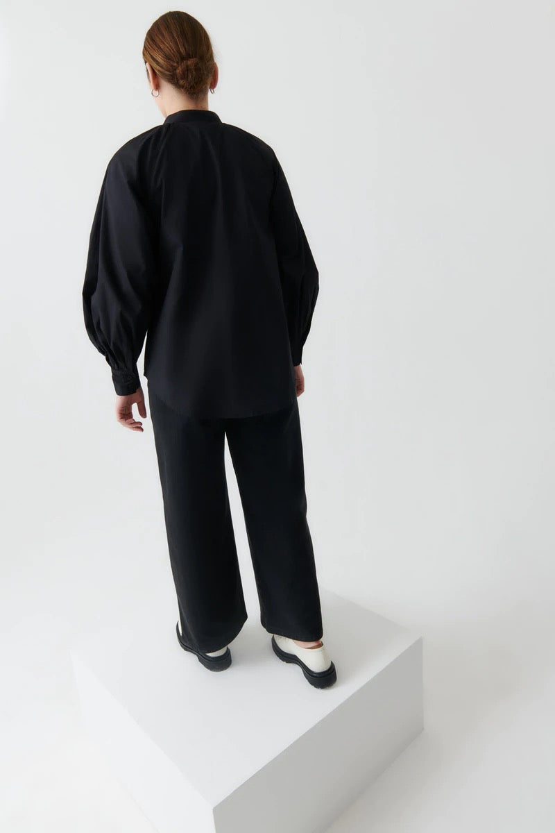 The model is wearing a Kowtow Ella Shirt - Black and pants.