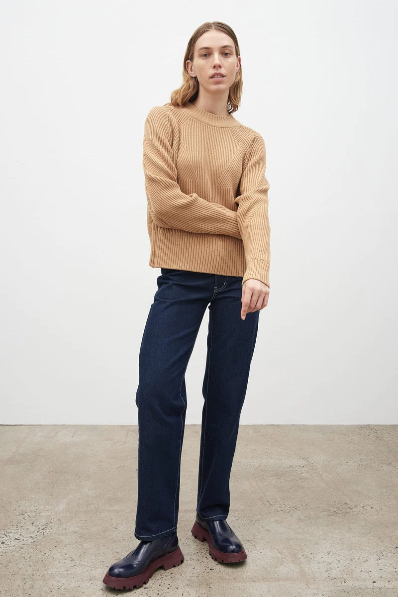 The model is wearing a Henri Crew - Beige sweater by Kowtow and blue jeans.