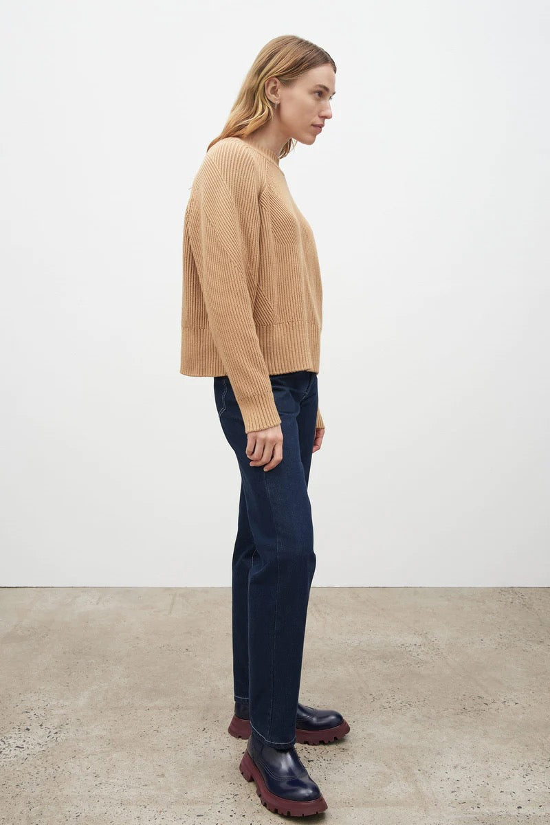 The model is wearing a Kowtow Henri Crew - Beige sweater and blue pants.