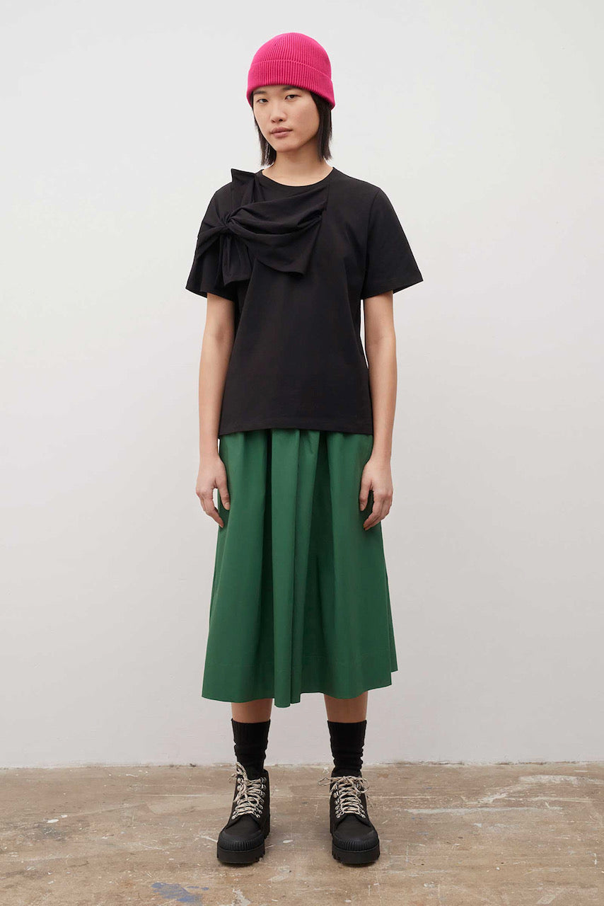 A woman wearing a Kowtow Knotted Tee - Black and green skirt.