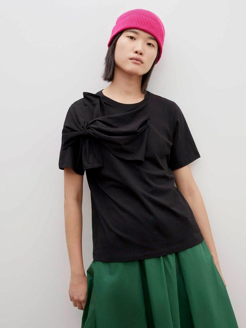 A woman wearing a Knotted Tee - Black t-shirt by Kowtow and green skirt.