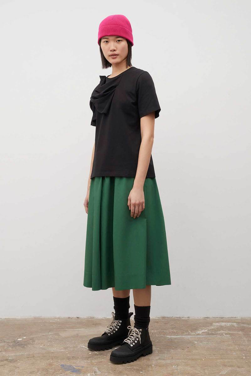 A woman wearing a Knotted Tee - Black by Kowtow and a green skirt.